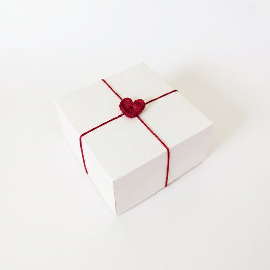 Balta dovanų dėžutė perrišta spalvota vija su nerta širdele.