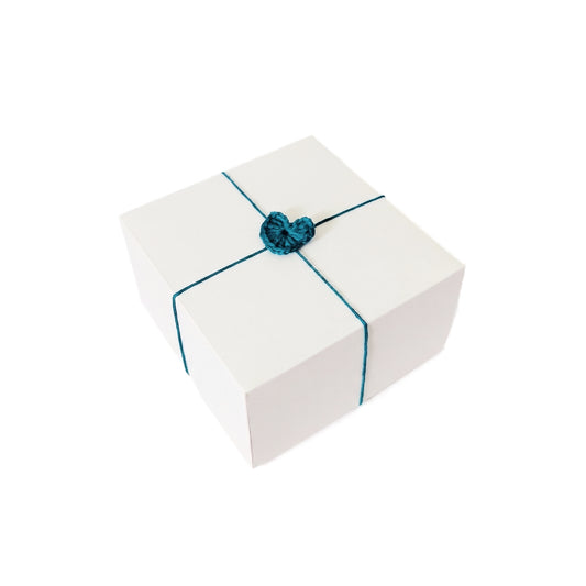 Balta dovanų dėžutė perrišta spalvota vija su nerta širdele.