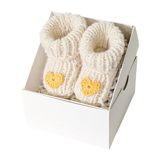 Rankų darbo balti vilnos tapukai kūdikiui su geltona širdele dovanų dėžutėje. Palankynų ir baby-shower dovana.